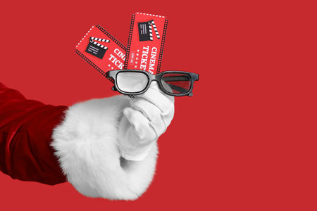 Santa's hand with cinema tickets and 3D glasses on red backgroundの写真素材