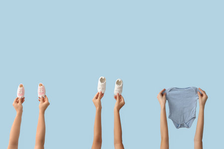 Female hands with baby bodysuit and shoes on blue background