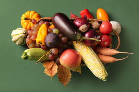 Wicker basket with fresh vegetables, fruits and autumn leaves on green background. Harvest festivalの写真素材