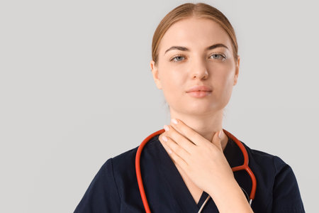 Female endocrinologist self-examining thyroid gland on gray background, closeup