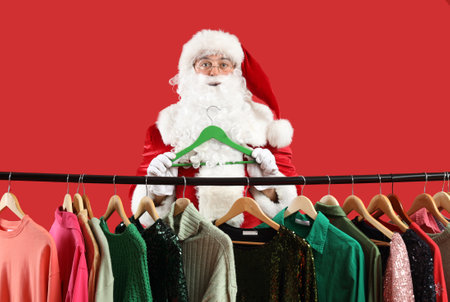 Santa Claus holding hanger near rack with different clothes on red backgroundの写真素材