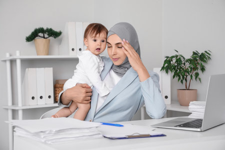 Young tired business Muslim mother in hijab with little baby working at homeの写真素材