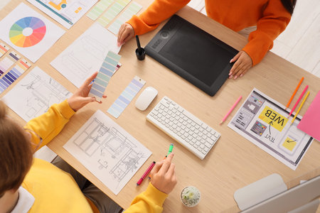 Couple of graphic designers working at table in office, top view