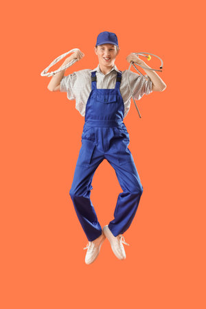 Jumping male plumber with hoses on orange backgroundの写真素材