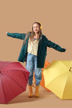 Cute teenage girl in headphones with different umbrellas on brown backgroundの写真素材