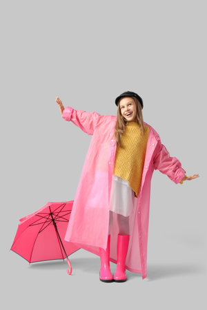 Cute teenage girl in raincoat with pink umbrella on gray backgroundの写真素材