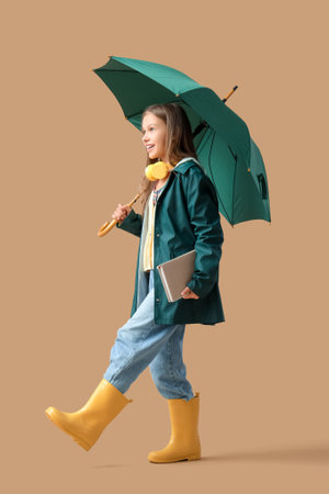 Cute teenage girl with green umbrella, book and headphones on brown backgroundの写真素材