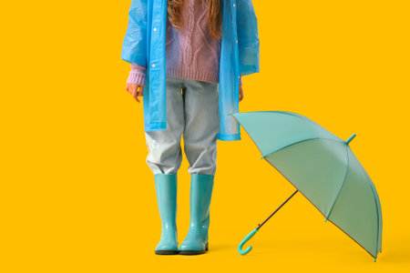 Teenage girl in raincoat with blue umbrella on yellow backgroundの写真素材