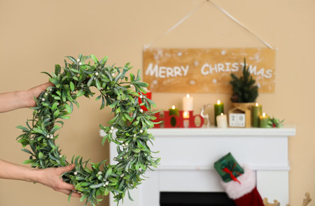 Female hands with Christmas mistletoe wreath in interior of decorated living room with white fireplaceの写真素材