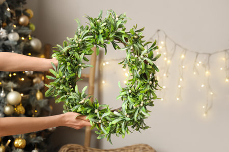 Female hands holding Christmas mistletoe wreath in living roomの写真素材