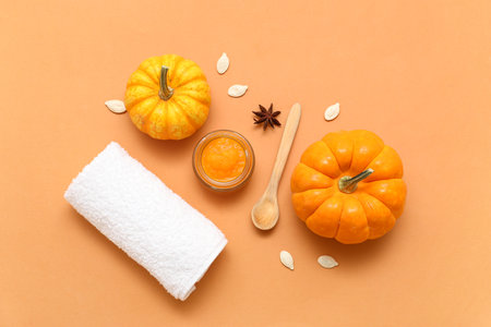 Jar of cosmetic pumpkin mask with seeds and towel on orange backgroundの写真素材