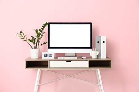 Stylish workplace with modern computer, houseplant and clock near pink wall in officeの写真素材