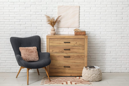 Chest of drawers, armchair and picture on white brick wall in room