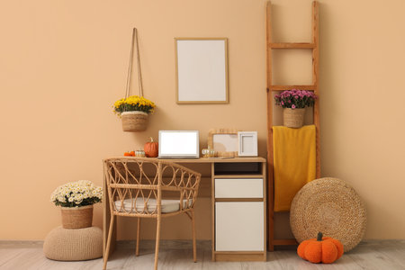 Workplace with autumn decoration, laptop and chrysanthemum flowers near beige wall in roomの写真素材