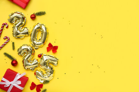 Figure 2025 made of foil balloons with Christmas balls, candy canes, gift boxes and fir branches on yellow backgroundの写真素材