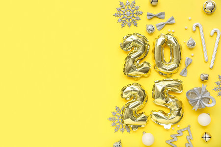 Figure 2025 made of foil balloons with Christmas decorations and gift box on yellow background