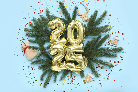 Figure 2025 made of foil balloons with Christmas decorations, fir branches and confetti on blue...