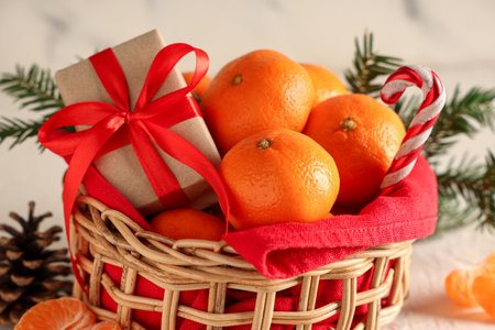 Wicker basket with sweet tangerines, gift box and decorations on white table near grunge wallの写真素材