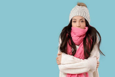 Frozen young woman in winter clothes on blue backgroundの写真素材