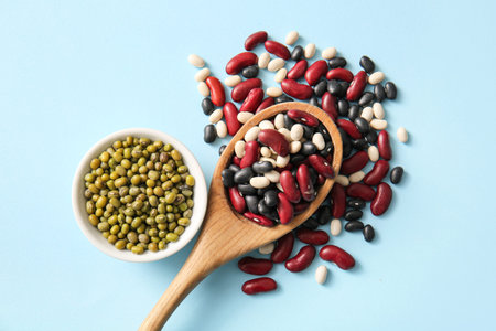 Spoon and bowl with different legumes on color background