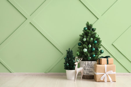 Small Christmas trees with gift boxes and decorative deer near green wallの写真素材