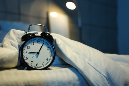 Retro alarm clock with blanket on bed in dark bedroom at night, closeupの写真素材