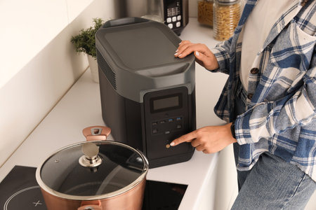 Young woman turning on portable power station in kitchenの写真素材