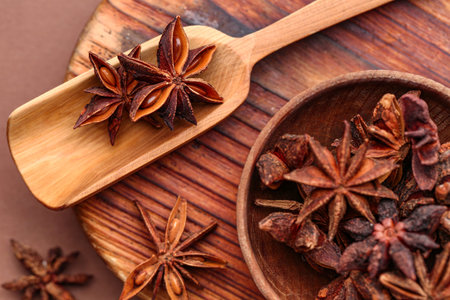 Wooden board with bowl of aromatic star anise and scoop on color background, closeup