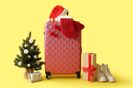 Suitcase with Christmas tree, decor and boots on yellow backgroundの写真素材