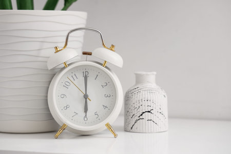 Retro alarm clock with plant and vase on table near light wall