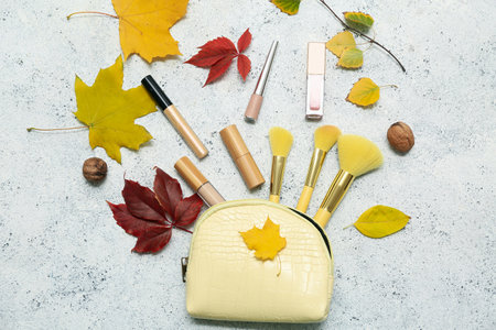 Composition with bag, decorative cosmetics, makeup brushes and autumn leaves on light backgroundの写真素材