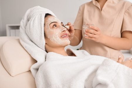 Cosmetologist applying mask onto young woman's face in beauty salon, closeupの写真素材