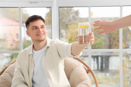Young man giving glass of lemon infused water to woman at home, closeupの写真素材