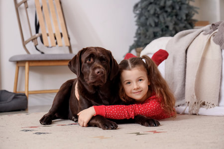 Cute happy girl in Christmas pajamas with Labrador dog lying at homeの写真素材