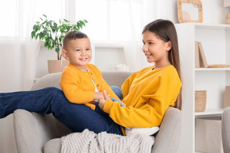 Teenage girl with her little brother hugging in armchair at homeの写真素材