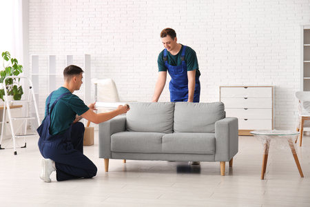 Male loaders wrapping sofa with stretch film in roomの写真素材