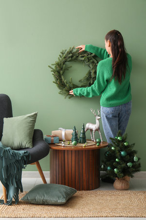 Young woman Christmas wreath on green wall hanging at home, back viewの写真素材