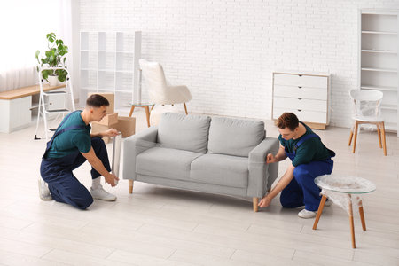 Male loaders wrapping sofa with stretch film in roomの写真素材