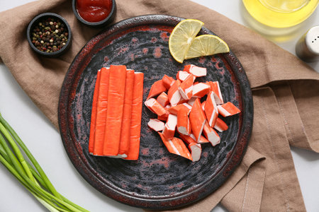 Plate with tasty crab sticks, slices of lemon and green onion on gray backgroundの写真素材