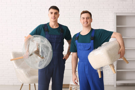 Male loaders holding wrapped furniture with stretch film in roomの写真素材