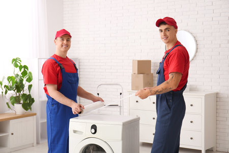 Male loaders wrapping washing machine with stretch film in roomの写真素材