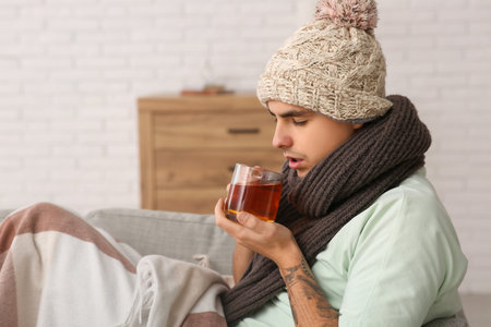 Ill young man with cup of tea at homeの写真素材