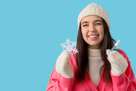 Young woman in winter clothes with serum and snowflake on blue background, closeupの写真素材