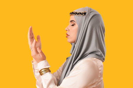 Beautiful Muslim woman in hijab praying on yellow background, closeupの写真素材