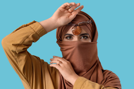 Beautiful Muslim woman in brown hijab on blue background, closeupの写真素材