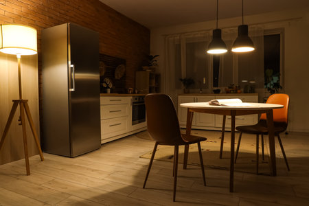 Interior of dark kitchen with counters, dining table and glowing lamps at nightの写真素材