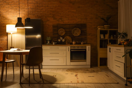Interior of dark kitchen with counters, dining table and glowing lamps at nightの写真素材