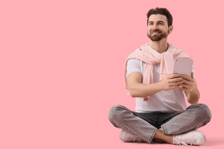 Handsome man with tablet computer sitting on pink backgroundの写真素材