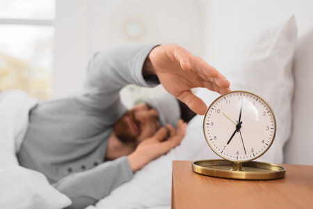 Morning of young man turning off alarm clock in bedroom, closeupの写真素材