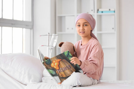 Little girl after chemotherapy with toy bear reading book at hospital. Childhood cancer awareness conceptの写真素材
